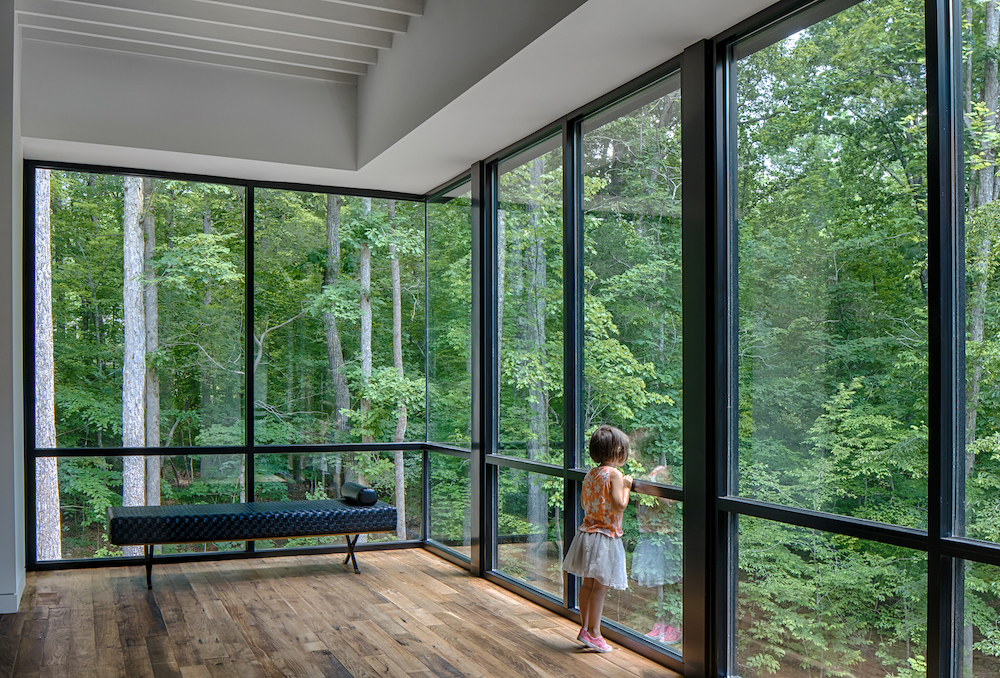 Girl looking into the woods from  floor to ceiling windows